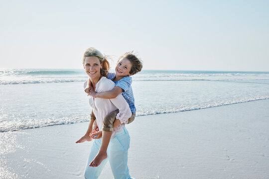 Happy mother carrying son piggyback on the beach