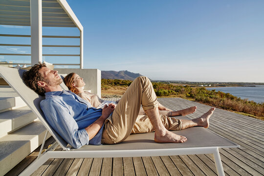 Couple lying on deck chairs at luxury beach house