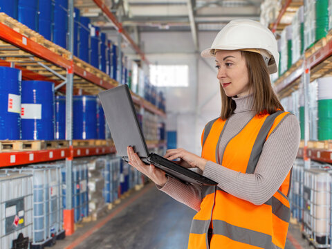 Warehouse logistics. Warehouse manager uses a laptop to monitor chemical inventory, warehouse operations, stock control and industrial supply chain management.