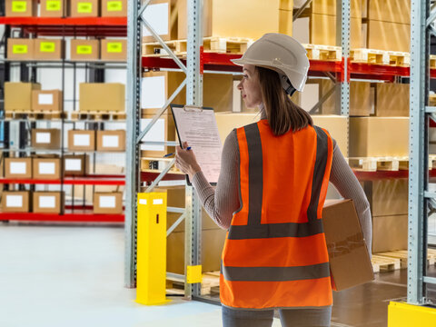 Warehouse logistics. Warehouse supervisor performs inventory audit with a checklist while inspecting storage racks, package handling and order fulfillment operations.