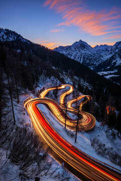 Car light trails stretching along winding road of Maloja Pass at dusk