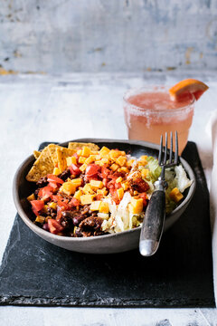 Bowl of nachos with, chili con carne, rice, lettuce, cheese, tomatoes and glass of refreshing paloma cocktail