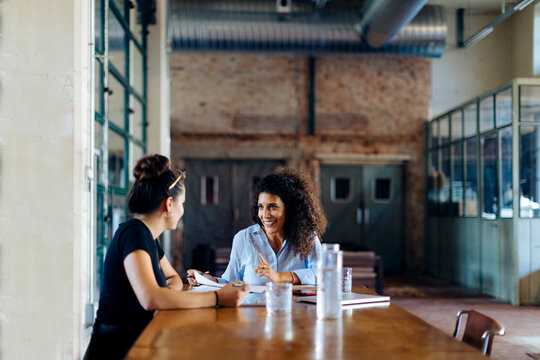 Two young businesswomen talking at conference table in loft office