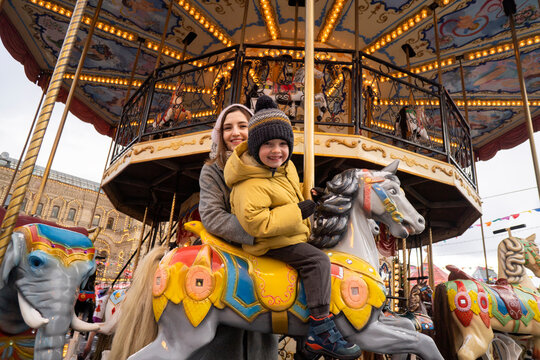 Smiling boy on carousel horse by mother in Christmas market
