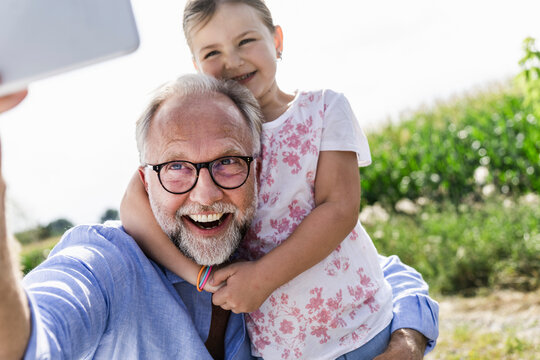 Mature man and little girl making fun selfies in the field