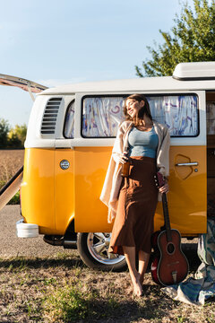 Pretty woman on a road trip with her camper, drinking beer, holding guitar