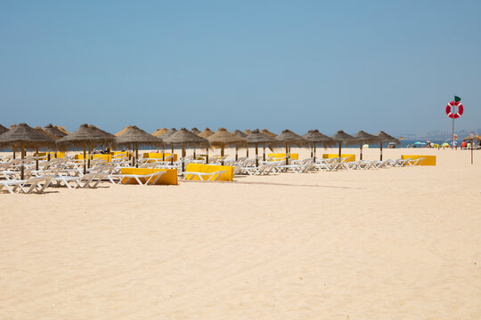 Thatched roof parasols and lounge chairs at beach against clear sky, Albufeira, Algarve, Portugal