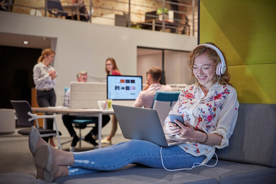Young woman working in modern creative office, usine laptop and headphones
