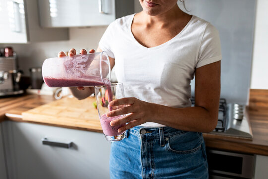 Woman pouring healthy milkshake in glass at home