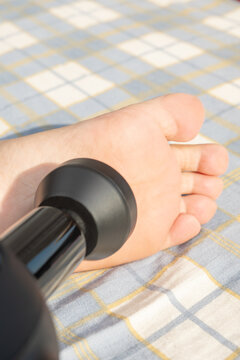 Massage gun acting on human sole on plaid picnic mat