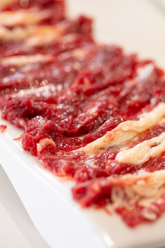 Fresh sliced raw beef arranged neatly on white plate