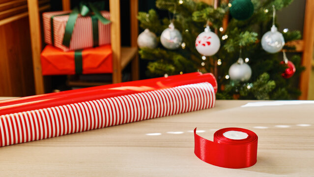 Christmas gifts preparation table with wrapping paper, gift, ribbon and xmas balls. Festive mood.