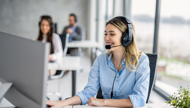 Happy young female call center agent with a headset working on a computer