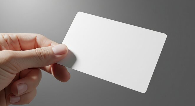 Close up of a bare hand holding a blank white rectangular card with rounded corners against a neutral gray backdrop