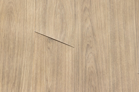 background of a damaged wood laminate flooring with lifted joint and construction defect