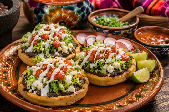 Traditional sopes topped with beans, cheese, lettuce, salsa, and crema, served on a rustic ceramic plate with vibrant fresh ingredients and authentic Mexican flavors.