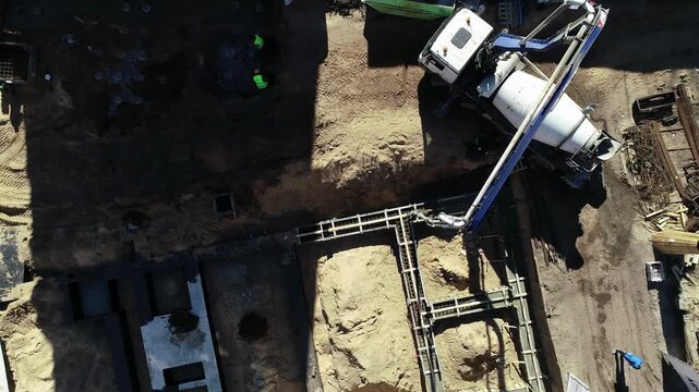 Latvia - 18 February 2023: Aerial view of a concrete mixer truck pouring concrete into foundation trenches at a construction site.