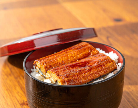 Japanese unadon grilled eel over rice in a black lacquer bowl with red lid on a wooden table