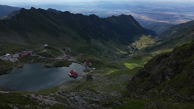 Static aerial view overlooking B&acirc;lea Lake with vehicles traveling along the Transfăgărășan road while hikers explore the surrounding mountain landscape.