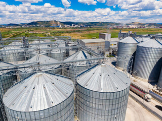 View of storage silos at a grain facility under a cloudy sky in a rural area near hills and mountains © DSMT