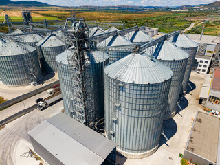 Grain storage facility and silos located in a rural area with agricultural land and mountains in the background © DSMT