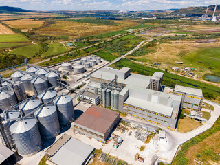 Large industrial site with storage silos and processing buildings in a rural area under a clear sky © DSMT