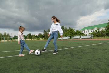 Obraz premium Young mother teaches girl soccer on green field, capturing motherhood in motion. Motherhood encourages learning, motherhood reflects care, and motherhood elevates sport storytelling campaigns.