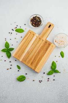 Wooden cutting board with basil and peppercorns on light background