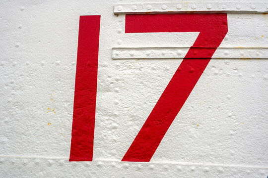 Bold red number 17 painted on a weathered white metal panel with visible rivets and texture