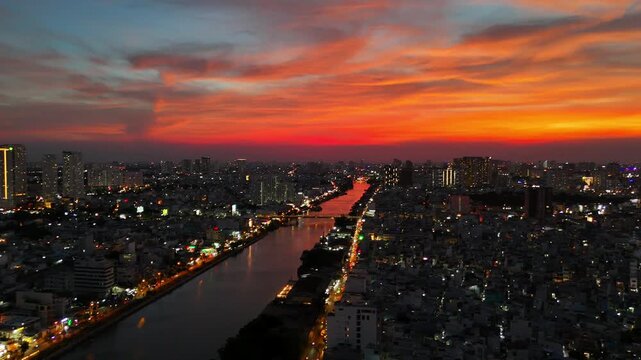 Panoramic drone shot of Ho Chi Minh City skyline, Ben Nghe Canal, and city lights at dramatic red sunset in District 4, Saigon Vietnam
