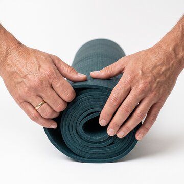 Close up of hands rolling a dark teal yoga mat on a white background Silhouette
