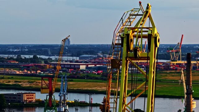 Riga, Latvia - 26 August 2025: Aerial view of the industrial port of Riga with large yellow cranes, shipping containers, and cargo ships along the riverbank.