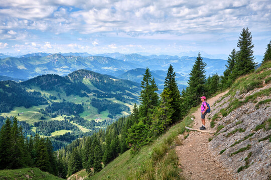 Active senior woman hiking along the scenic ridge of the Nagelfluh mountain range in the Allgaeu Alps with panoramic alpine views on a sunny summer day. Oberstaufen-Steibis, Allgaeu, Bavaria, Germany