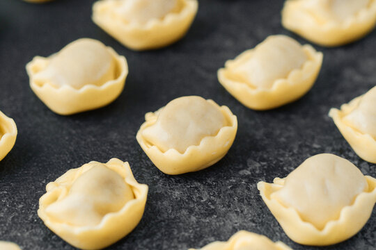 Diagonal scattered raw cappelletti pasta on dark background close up
