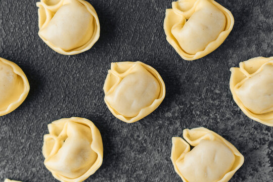 Diagonal scattered raw cappelletti pasta on dark background close up