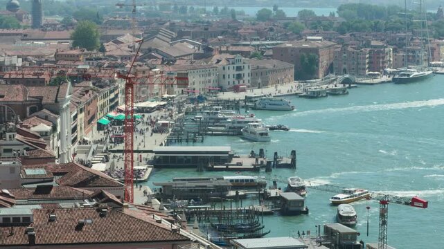 Boats navigate the blue lagoon past a busy Venetian waterfront with tourists and a red construction crane. This dynamic urban energy highlights the ongoing preservation of ancient heritage destination