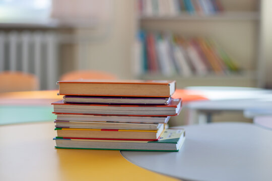 Stack of colorful books on desk in classroom. Education, learning and academic development. Back-to-school, preparation for lessons, pursuit of knowledge.