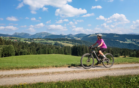 Active senior woman riding an e-mountain bike on a scenic alpine trail beneath the Nagelfluh mountain range on a sunny summer day. Oberstaufen, Allg&auml;u, Bavaria, Germany.