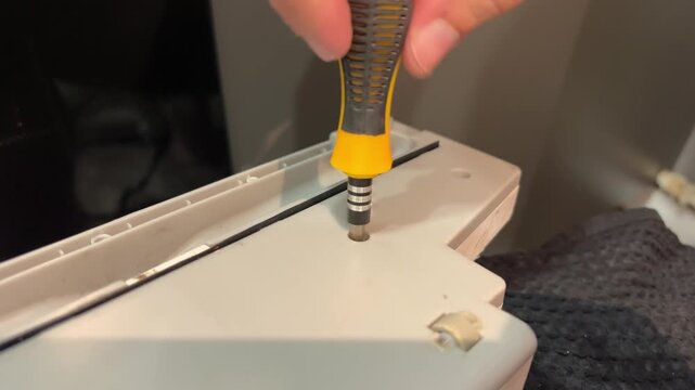 Close-up of hands using a screwdriver to repair a plastic household component, DIY maintenance, assembly and practical workshop work.