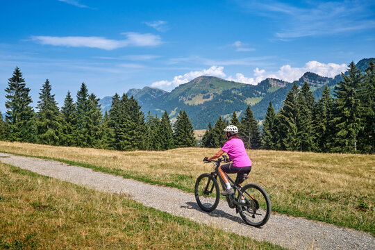 Active senior woman riding an e-mountain bike on a scenic alpine trail beneath the Nagelfluh mountain range on a sunny summer day. Oberstaufen, Allg&auml;u, Bavaria, Germany.