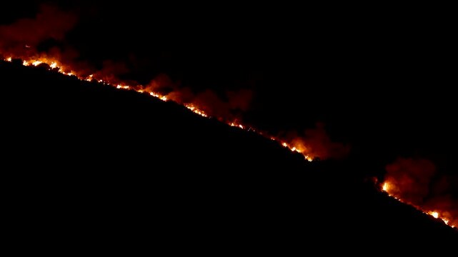 Bright flames and thick smoke consume a dark mountain ridge during a severe nighttime wildfire. Such devastating disasters highlight the urgent threats of climate change and extreme drought.