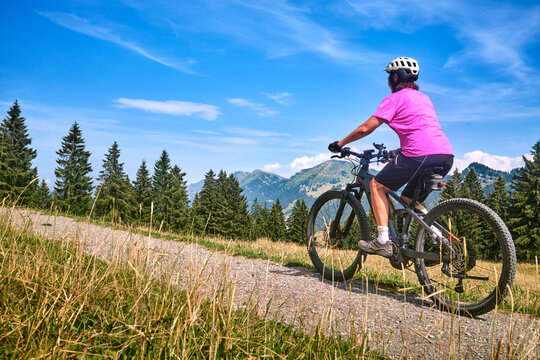 Active senior woman riding an e-mountain bike on a scenic alpine trail beneath the Nagelfluh mountain range on a sunny summer day. Oberstaufen, Allg&auml;u, Bavaria, Germany.