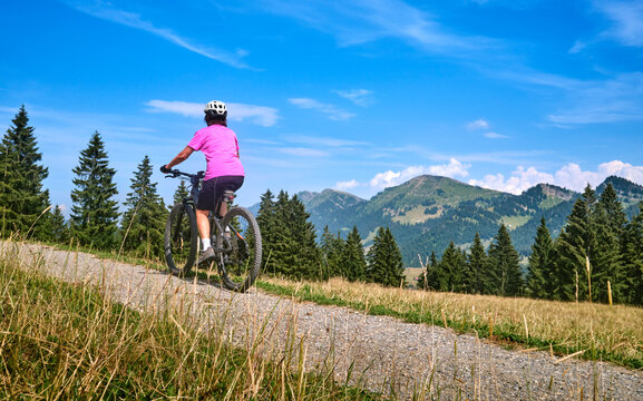 Active senior woman riding an e-mountain bike on a scenic alpine trail beneath the Nagelfluh mountain range on a sunny summer day. Oberstaufen, Allg&auml;u, Bavaria, Germany.