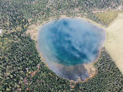 Aerial view of the circular Lac de Serviere surrounded by dense coniferous forests and grassy slopes in the volcanic landscape of Orcival, Auvergne-Rhone-Alpes, France.