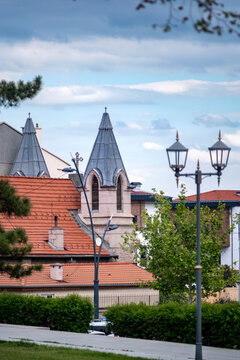 Church spires with gothic towers. The church rise over rooftops in a Konya. Photo framed by street lamp. Ideal for travel, editorial, religion, and European tourism content.