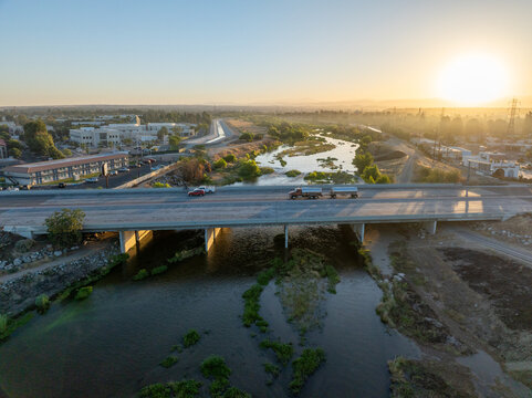 Aerial view of the Kern River flowing under a bridge with vehicles during golden hour in Bakersfield, California, United States.
