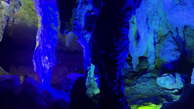Deep blue illuminated stalactites inside natural limestone cavern. Exploring mystical underground cave formations with geology and spelunking adventure concept.