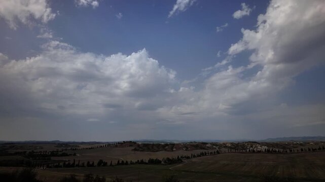 Fast moving clouds cast shadows over the rolling hills and iconic cypress trees of the Tuscan countryside. Such a majestic rural landscape inspires deep tranquility and celebrates Italian travel.