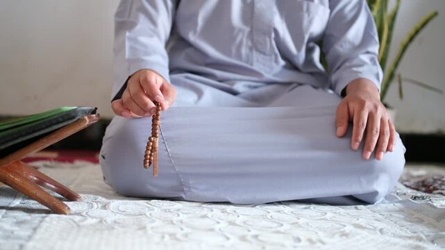 Close-up of hands reciting dhikr using prayer beads with a blurred background. Hands reciting dhikr. A man reciting dhikr while holding a prayer bead. Front view photo
