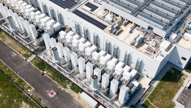 Aerial view of diesel backup generators at a data center facility, featuring rows of white cooling units and exhaust stacks, with solar panels on the building roof in Milan, Lombardy, Italy.